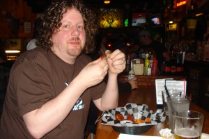 Ted and The Gin Mill's wings. A man with long curly hair and a beard eating chicken wings, with sauce on his hands and face.