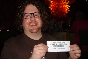 Ted's Big Win A picture of a man with long curly hair, a beard and glasses holding up a white ticket with a cash sum printed on it.