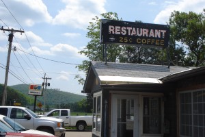 25-cent Coffee A picture of the outside of a small diner, with cars in the parking lot and blue sky behind, and a sign reading "Restaurant 25 cent coffee"