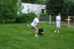Kan Jam 1 A picture of two men on a green lawn on either side of a black drum, one throwing a frisbee.